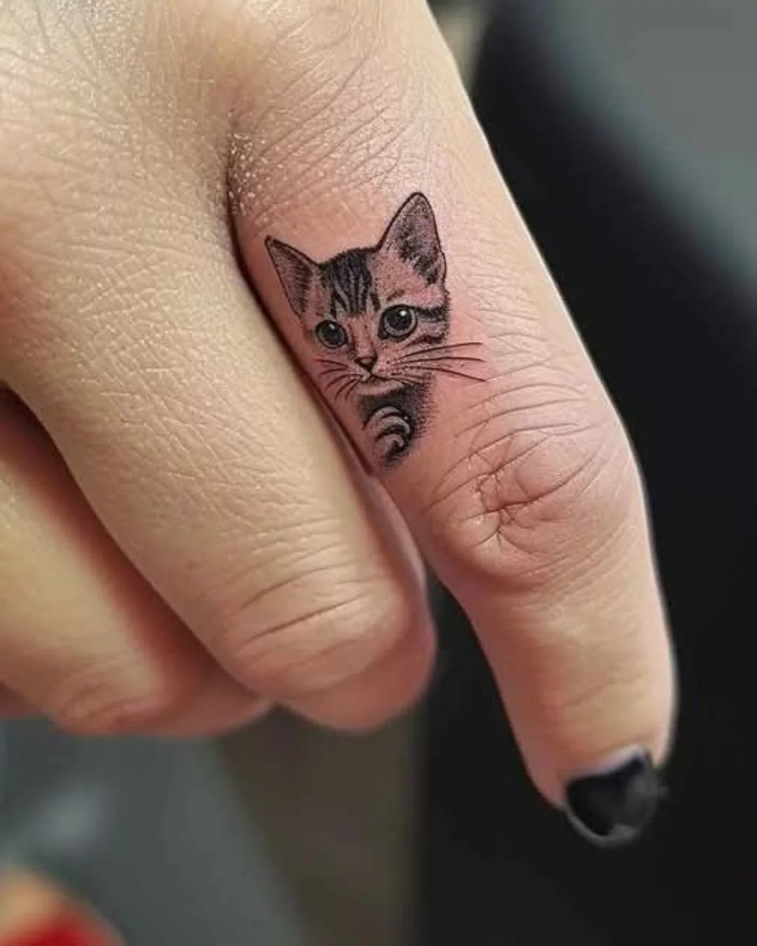 Small kitten face tattoo on the side of a person's finger.