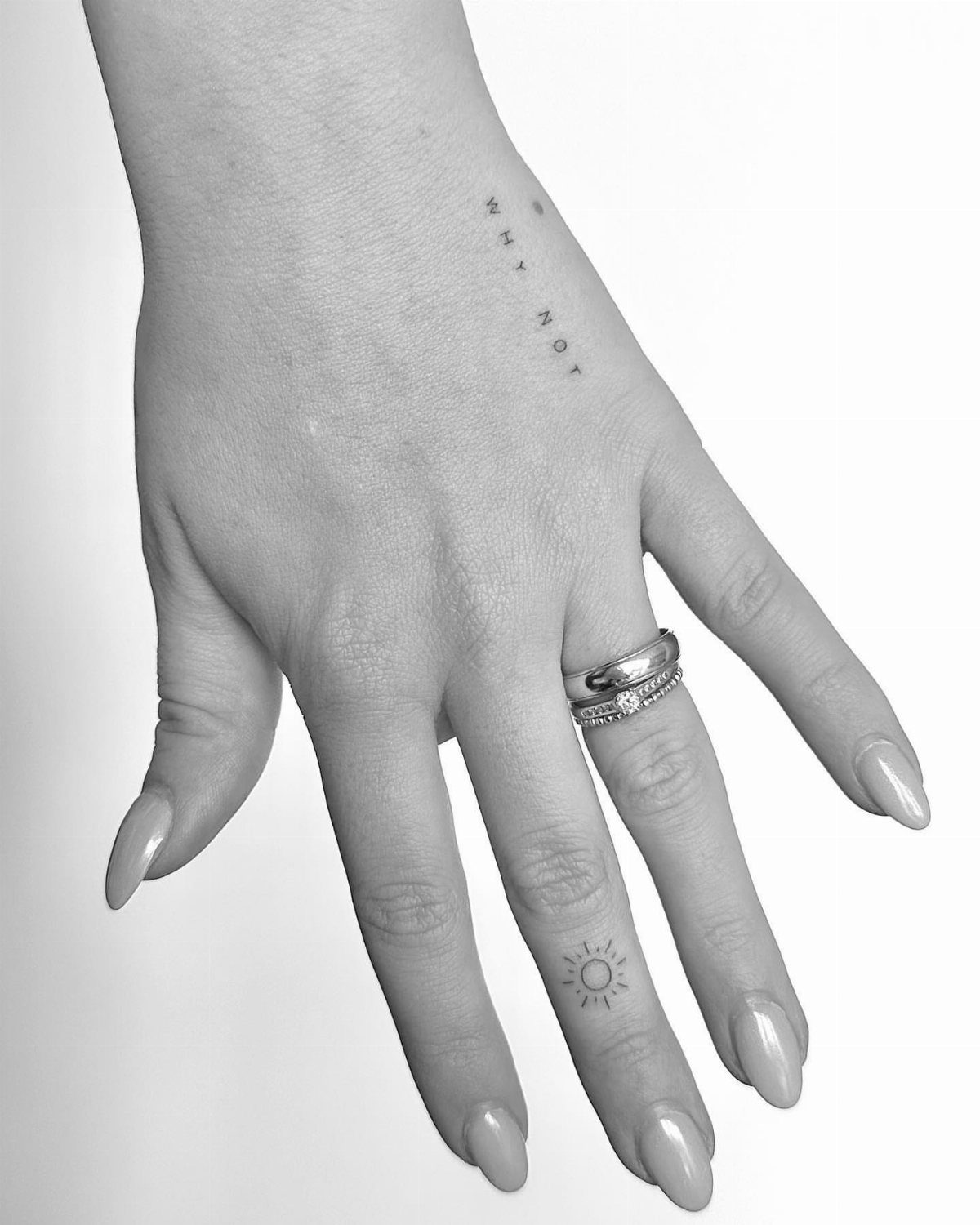 Hand with a small minimalist sun tattoo on the ring finger and silver ring.