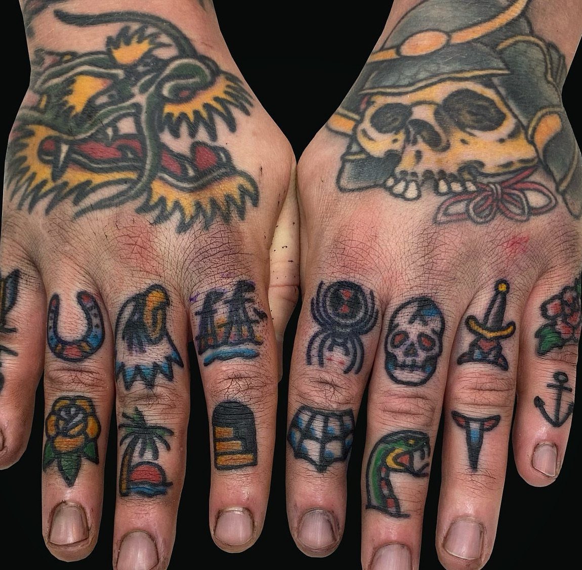 Hands with traditional finger tattoos including a skull, dagger, and nautical anchor.