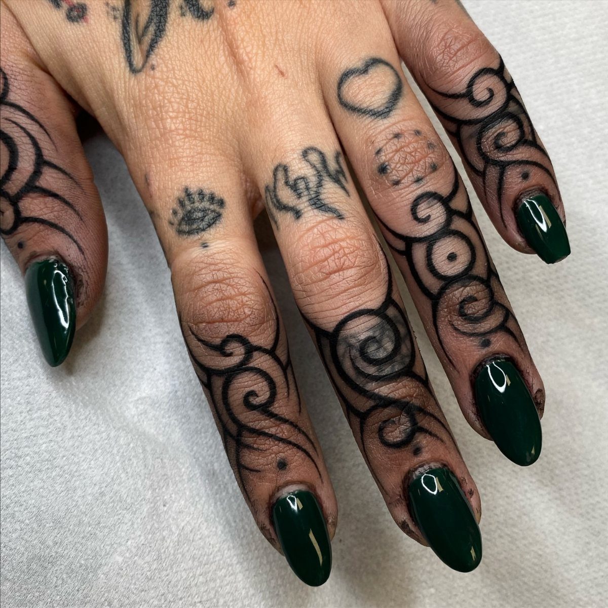 Hand with dark green nails and bold black tribal swirl tattoos on fingers