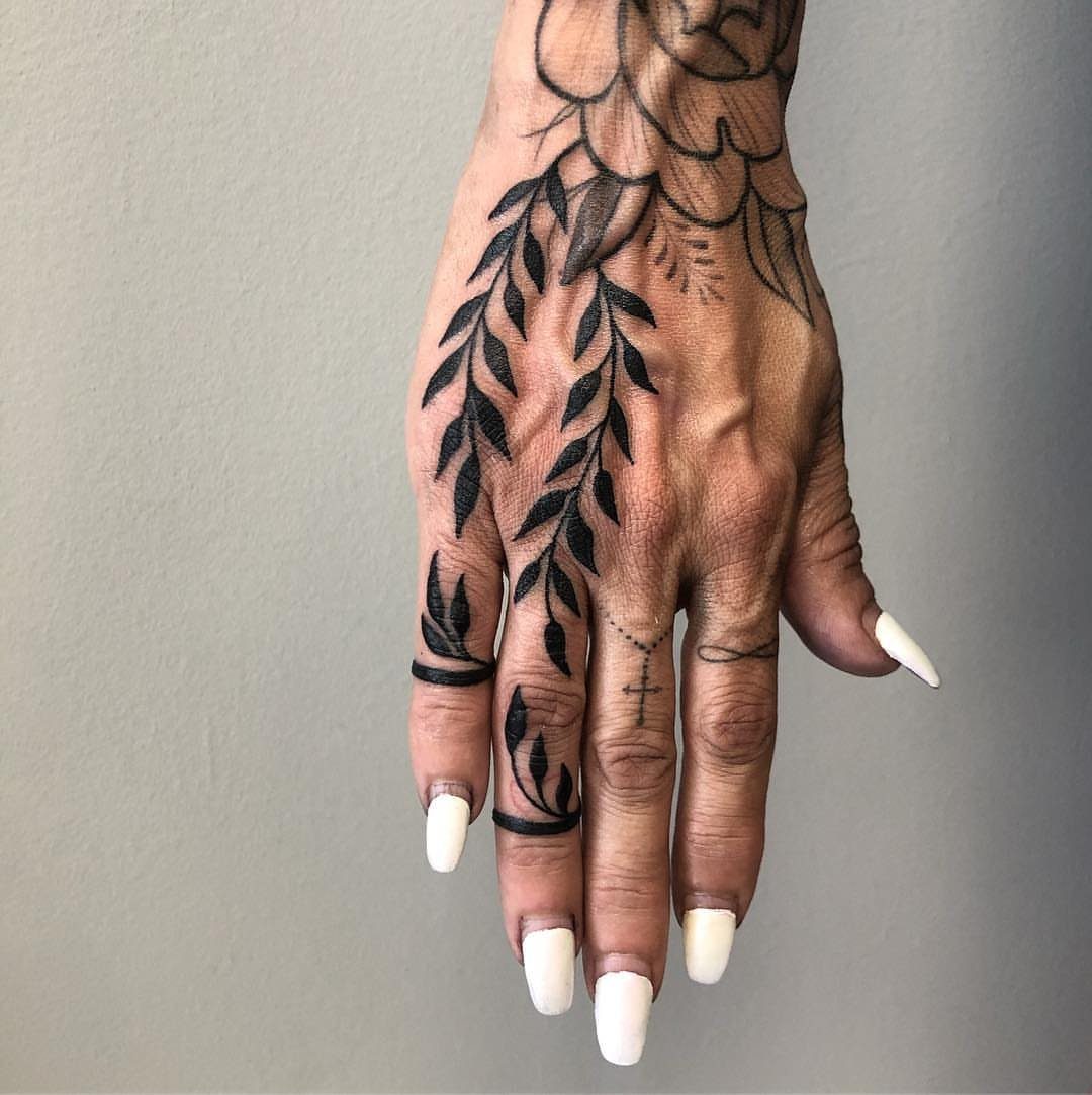 Hand with black ink tattoos featuring leafy vines wrapping around the fingers