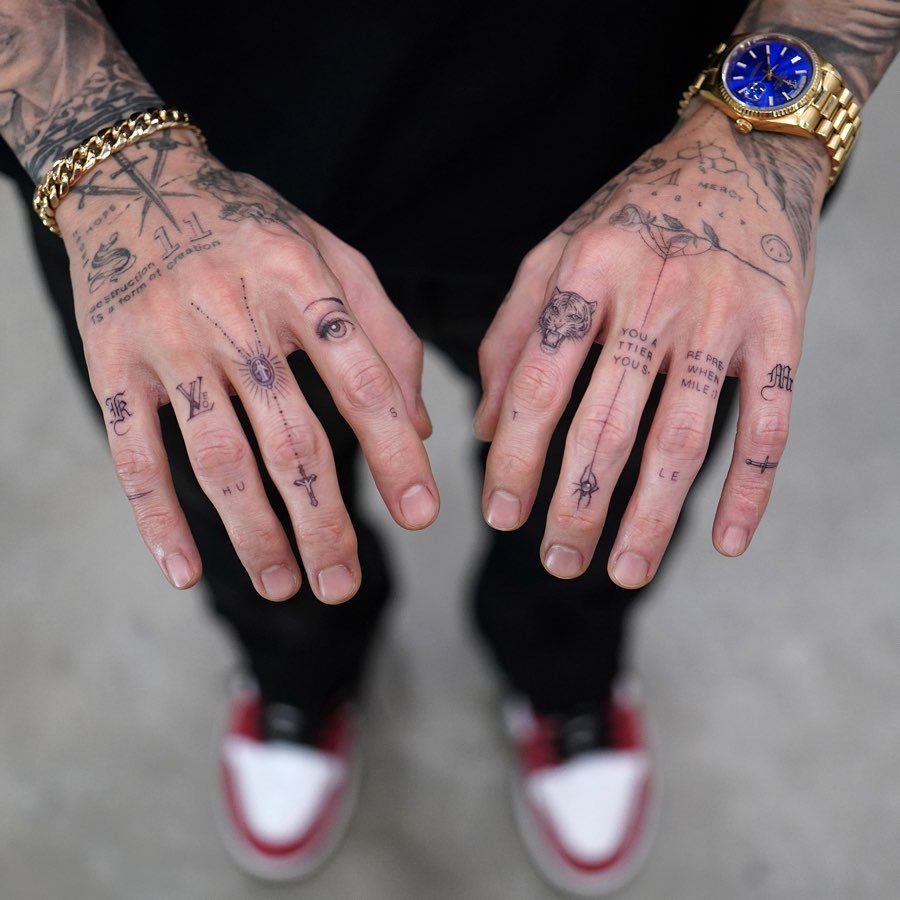 Tattooed hands showing word script tattoos on knuckles and various finger symbols.