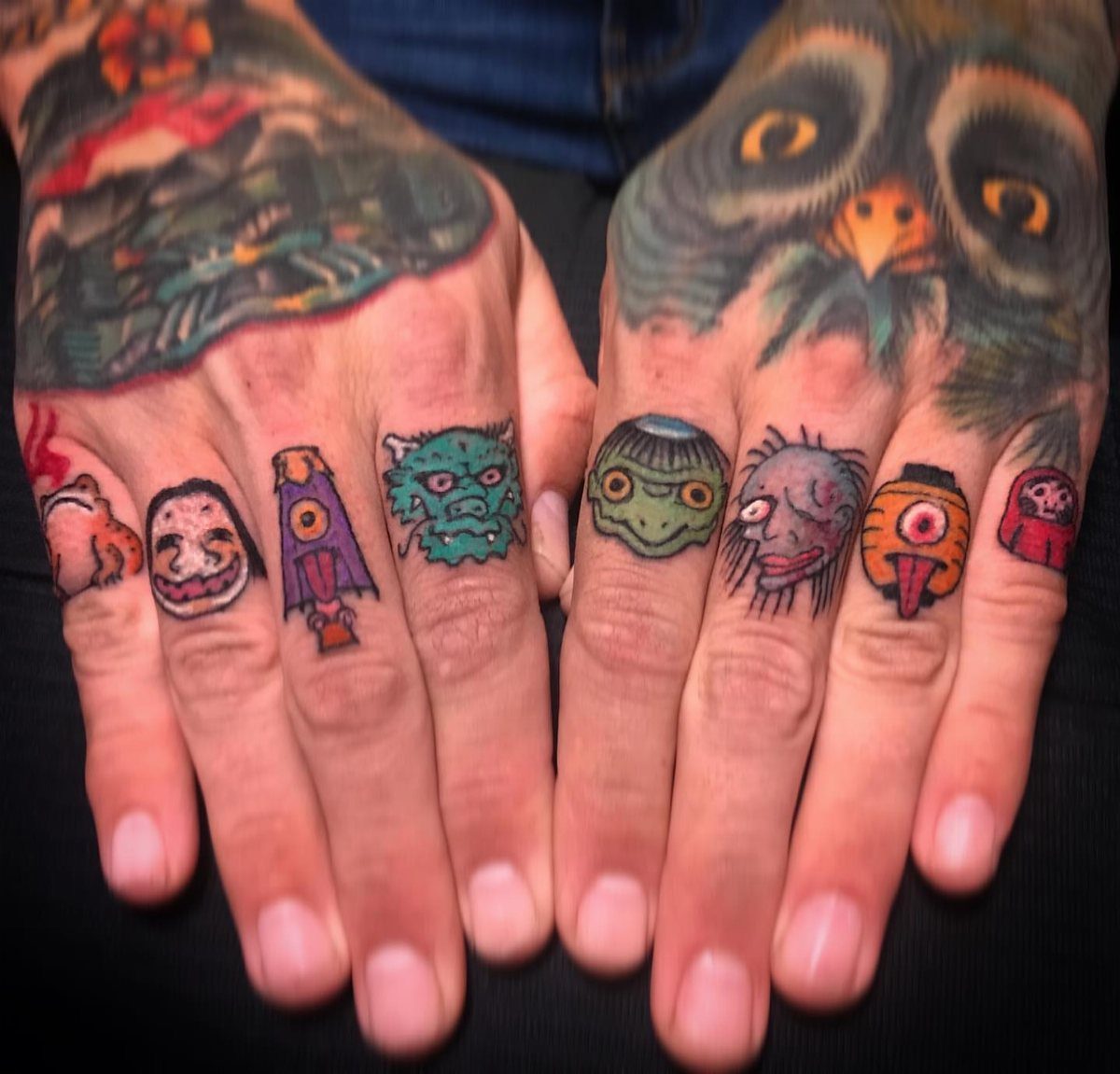Colorful creature and mask tattoos on the fingers and hands of a person