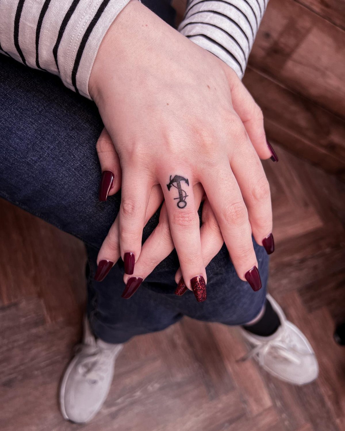 Small black anchor tattoo on a middle finger with long dark red nails.