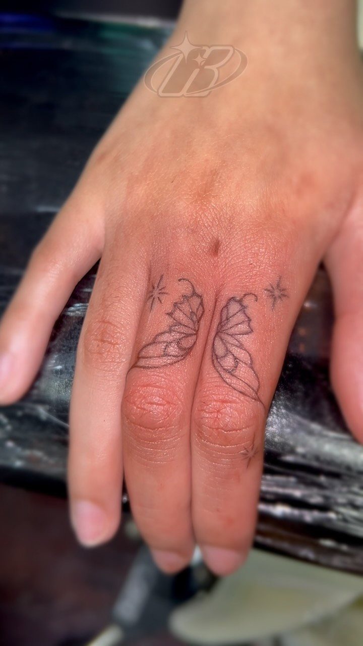Butterfly tattoo split across the middle and ring fingers with small sparkling stars.