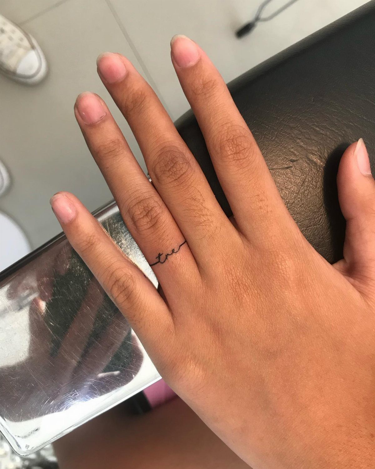 Hand with a small cursive word tattoo on the ring finger