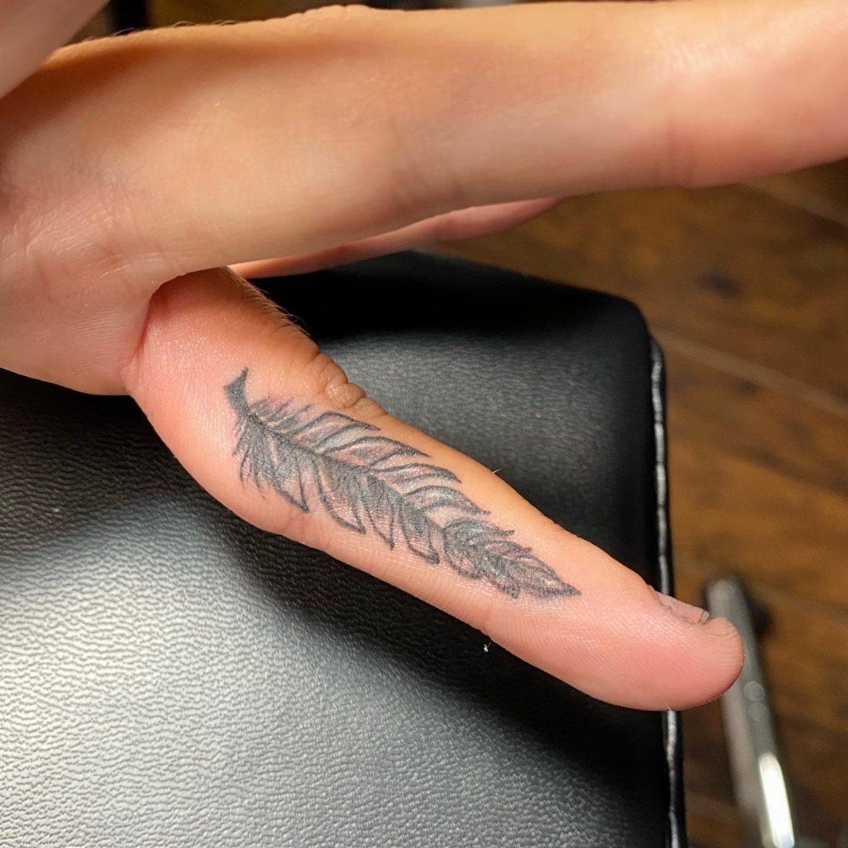 Feather tattoo on a person's finger resting on a black surface