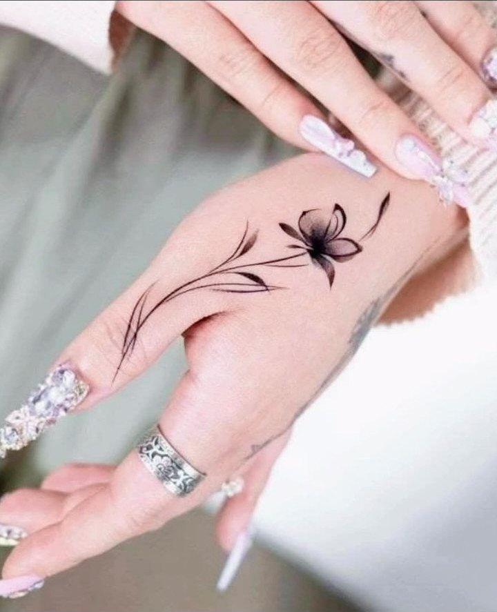 Woman's hand with a black floral tattoo extending onto her index finger.