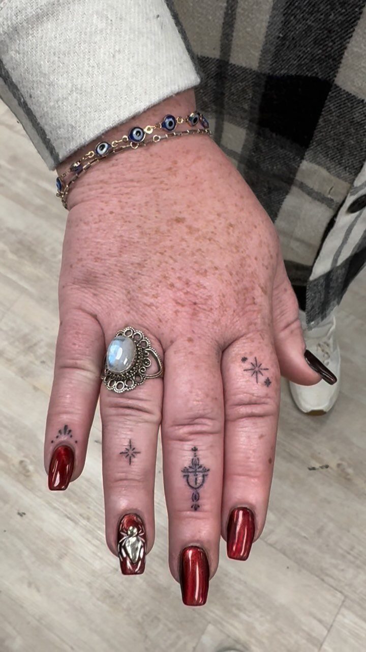 Hand with red nails featuring small black finger tattoos and an evil eye bracelet.