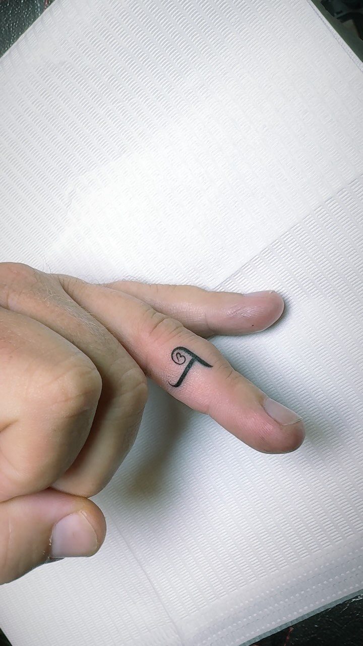 Stylized letter T tattoo on the side of a person's index finger.