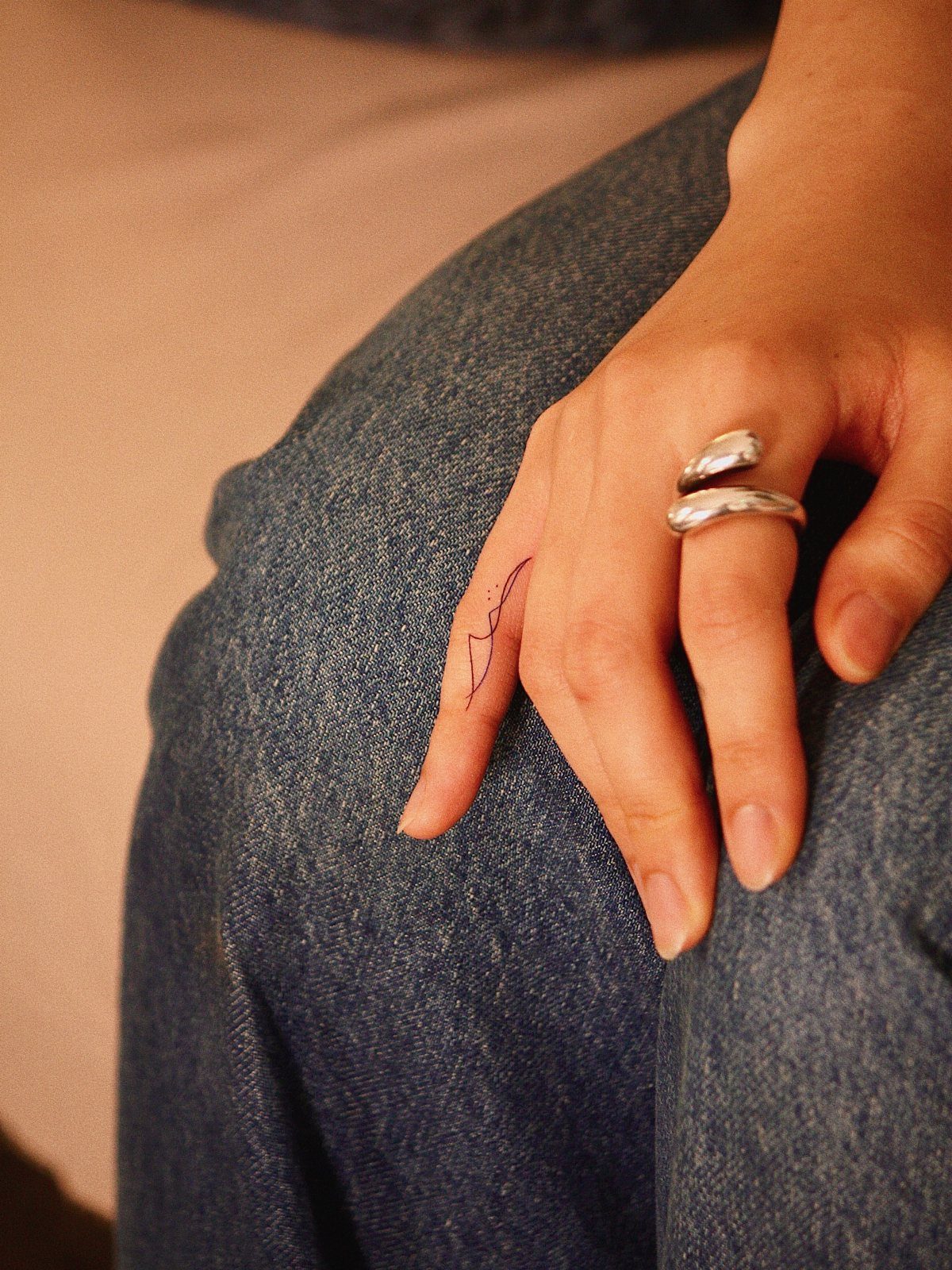 Hand with a small black line tattoo on the index finger and silver ring