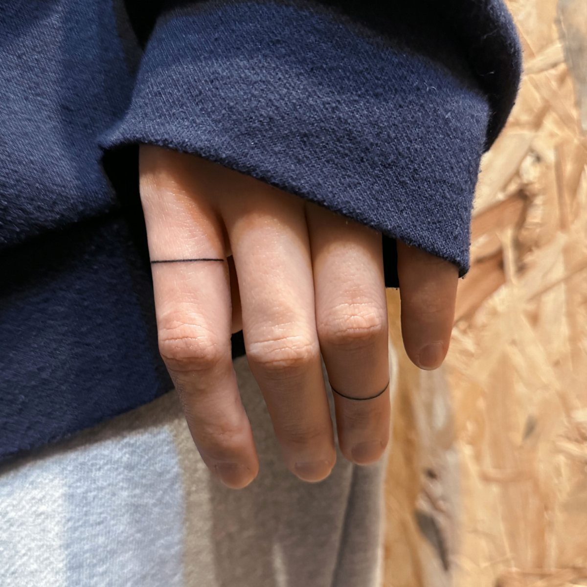 Hand with thin black line tattoos wrapping around two fingers like rings.