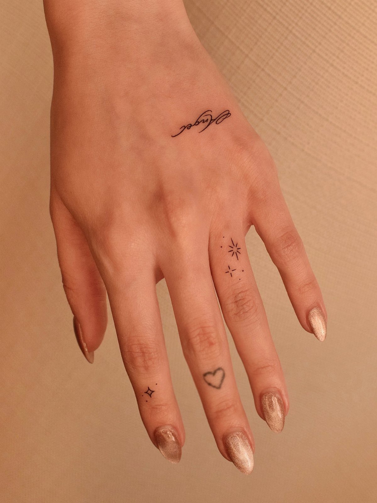 Woman's hand with small heart and star finger tattoos and gold nails