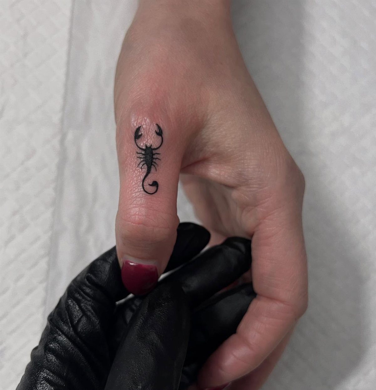 Small black scorpion tattoo on the side of a woman's thumb
