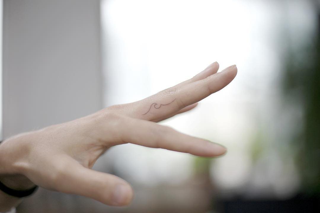 Small minimalist wave tattoo on the side of a person's index finger