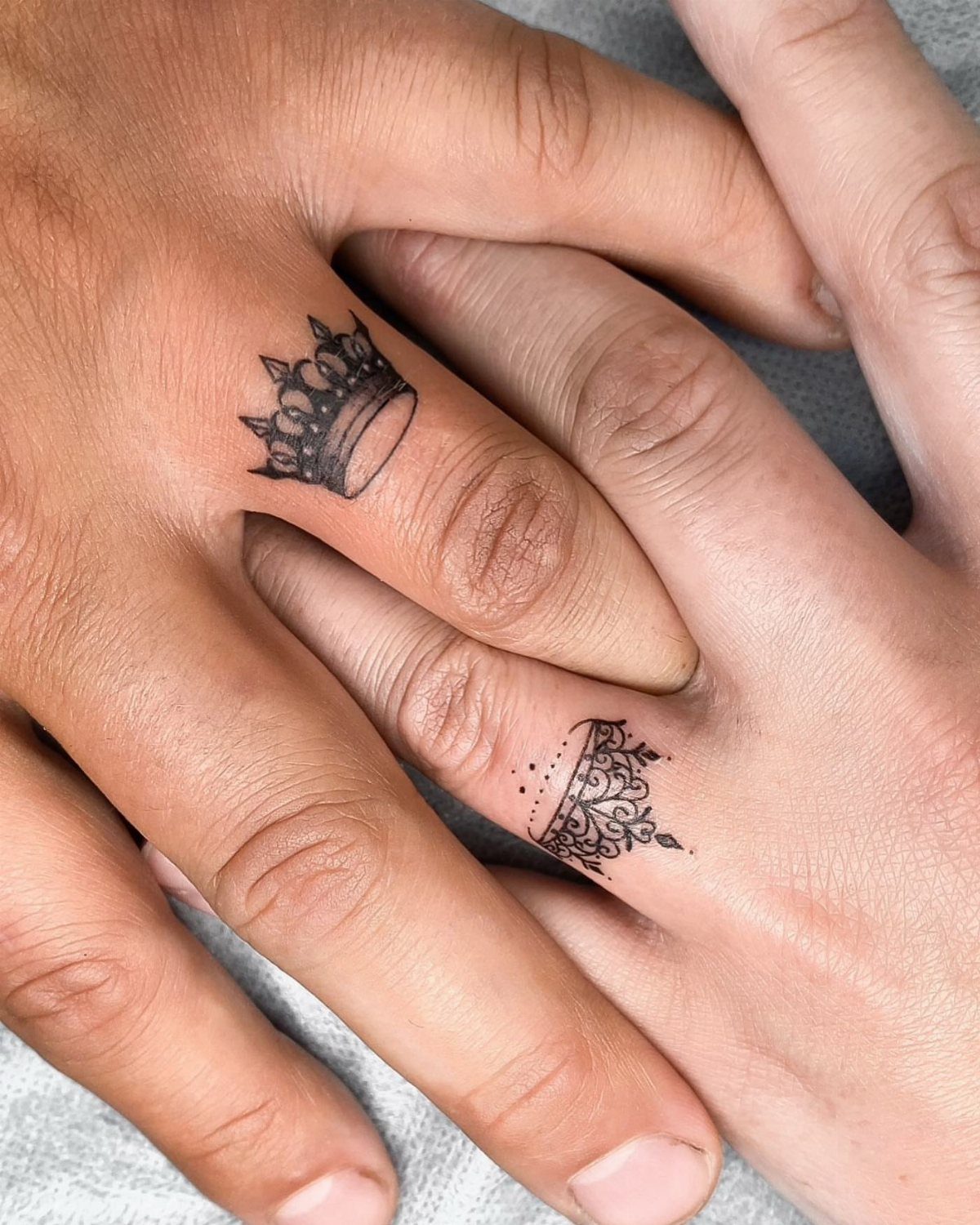 Two small black crown tattoos on the sides of fingers on intertwined hands.