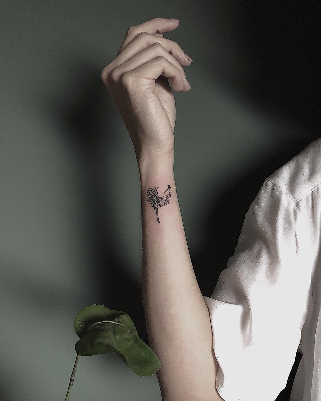 Small black dandelion tattoo on the inner wrist of a person's arm.