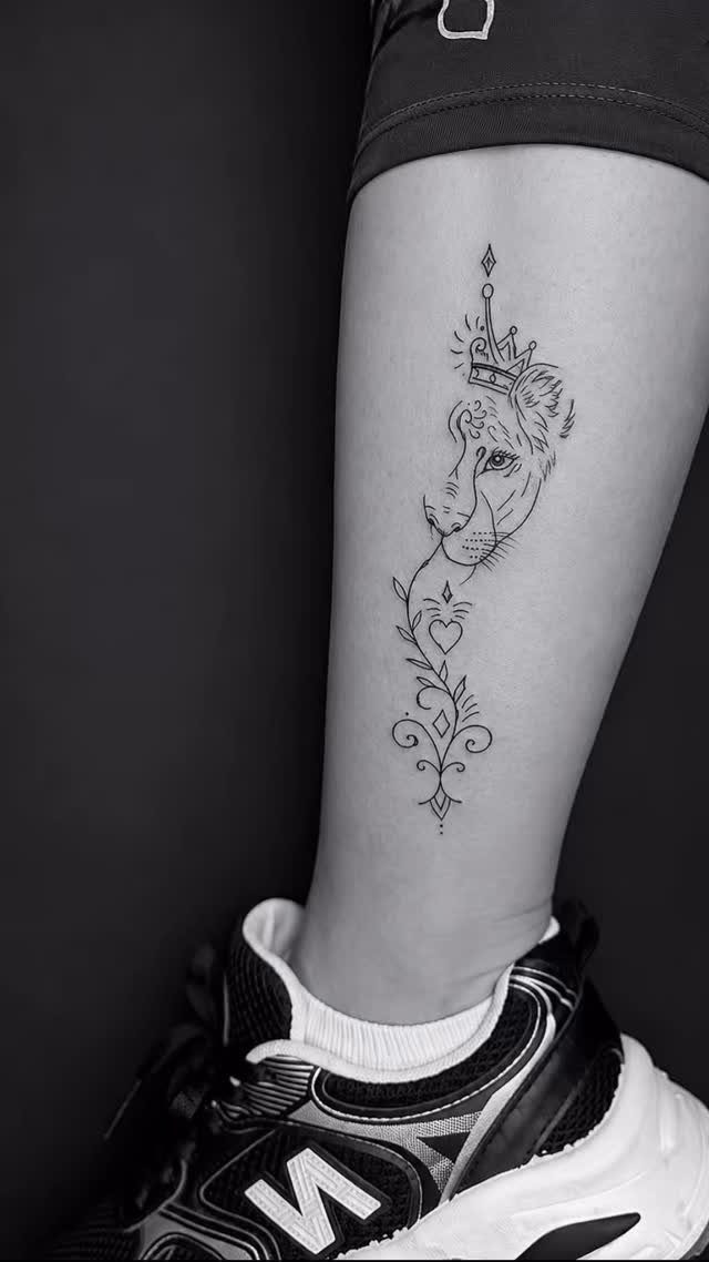 Lion head tattoo wearing a crown on a person's lower leg.
