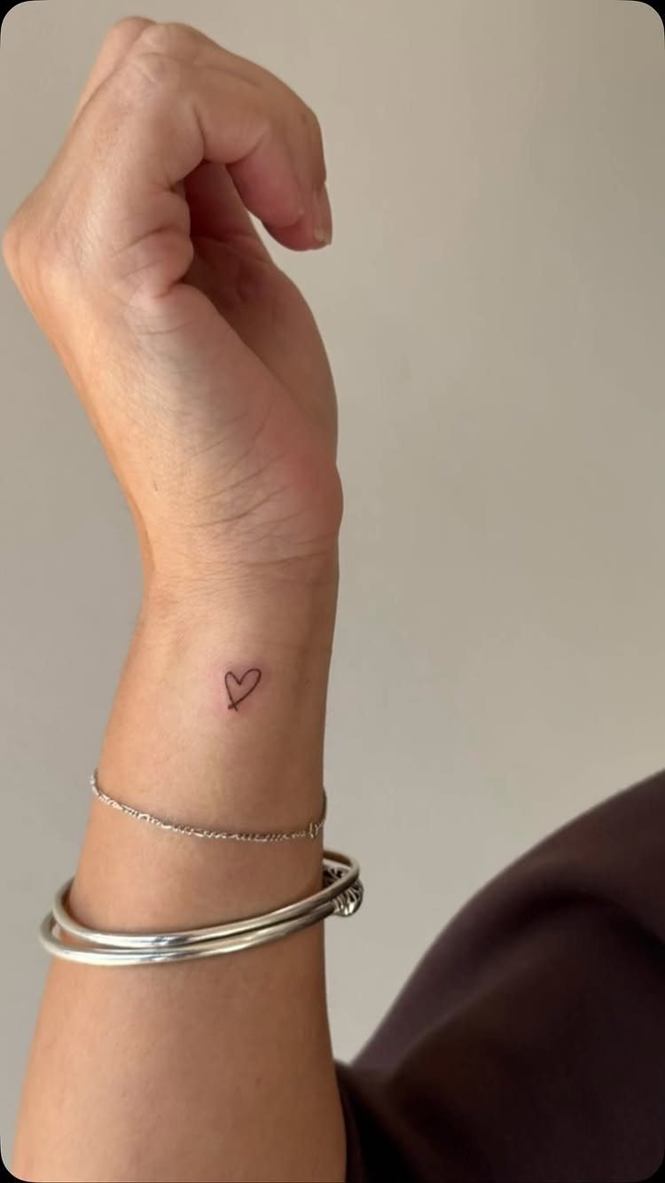 Small red heart tattoo on a wrist with silver bracelets.