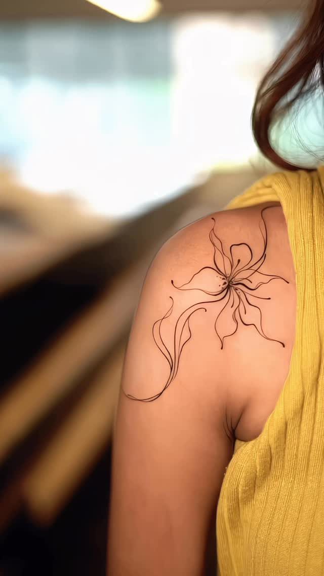 Stylized flower tattoo with flowing lines on a person's shoulder