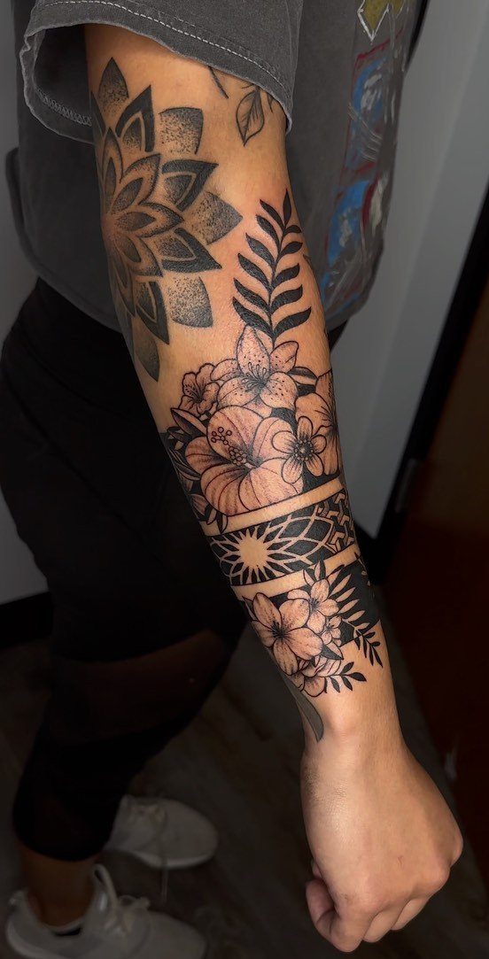 Forearm tattoo with a mandala, flowers, and geometric patterns in black ink.