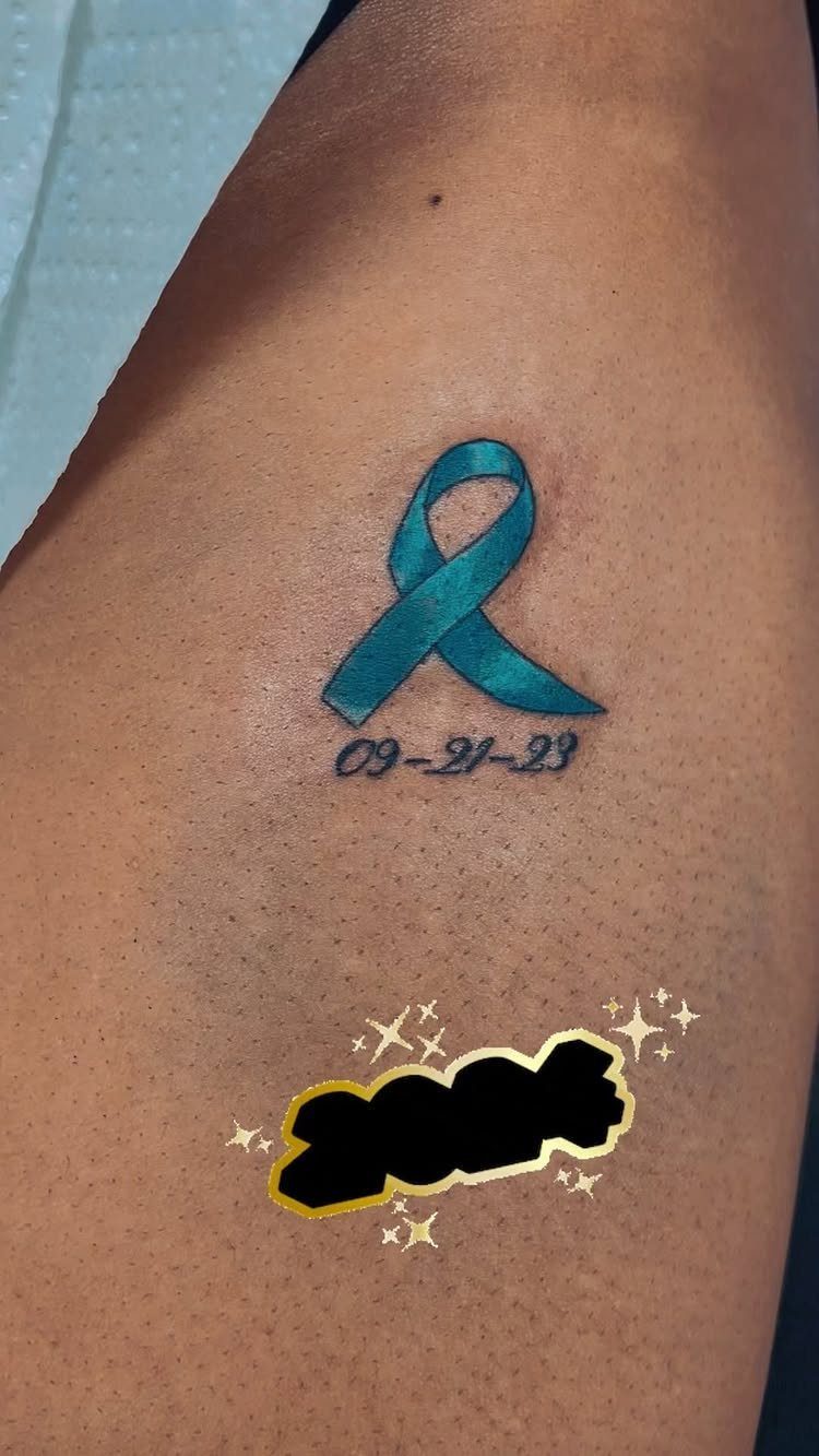 Teal awareness ribbon tattoo with a date on a person's skin.