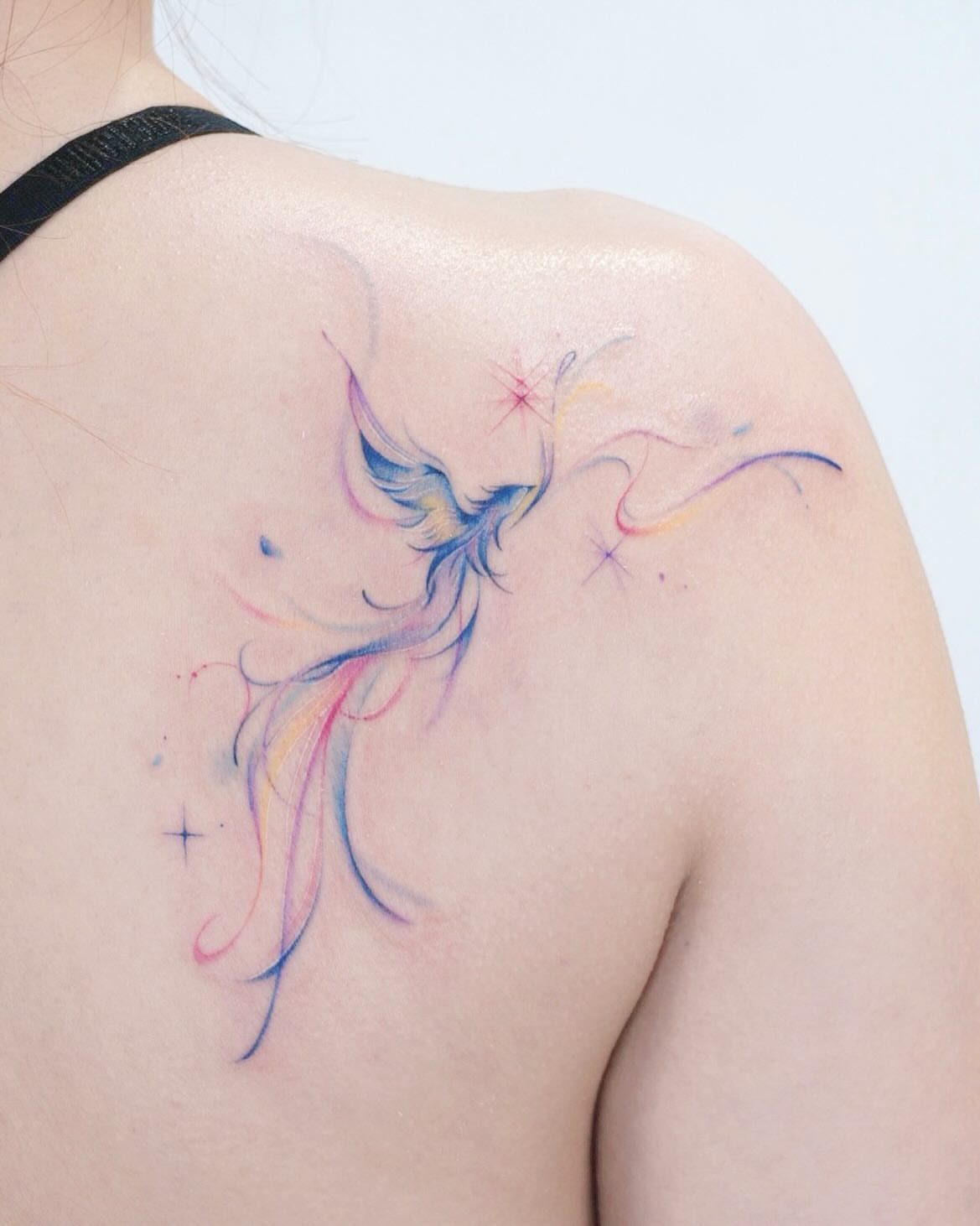 Watercolor phoenix tattoo with blue and pink hues on a person's shoulder.