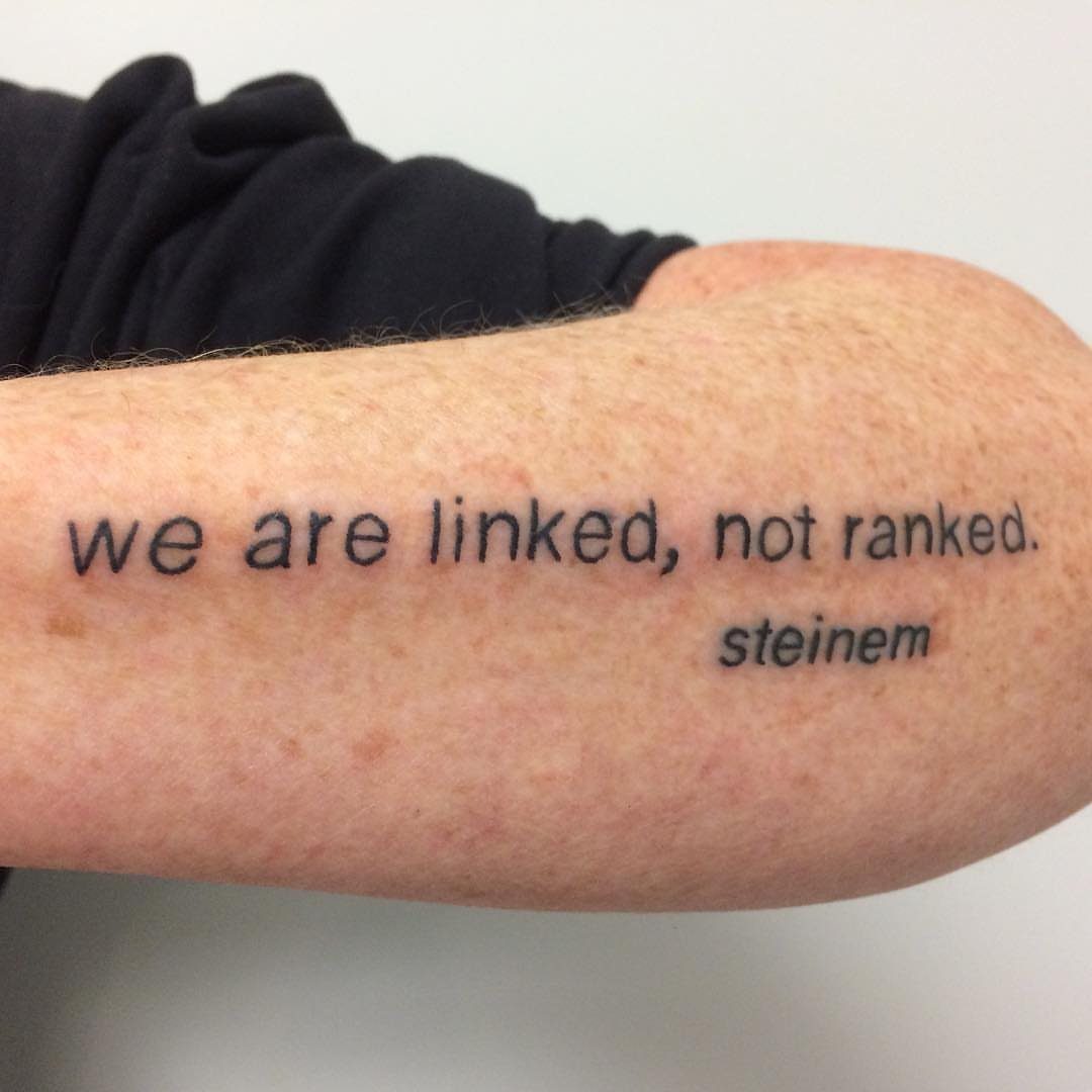 Black ink quote tattoo on an arm reading we are linked, not ranked.