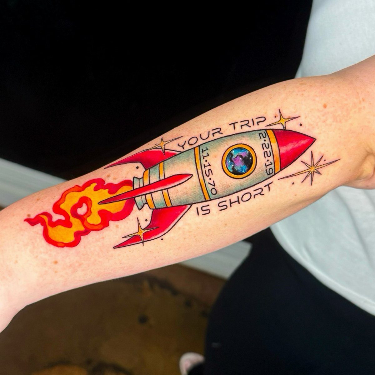 Rocket ship tattoo on a forearm with red flames and text