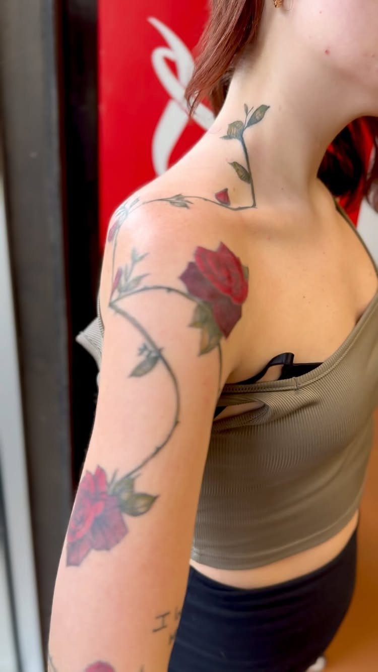 Red rose vine tattoo winding from a woman's upper arm up to her neck
