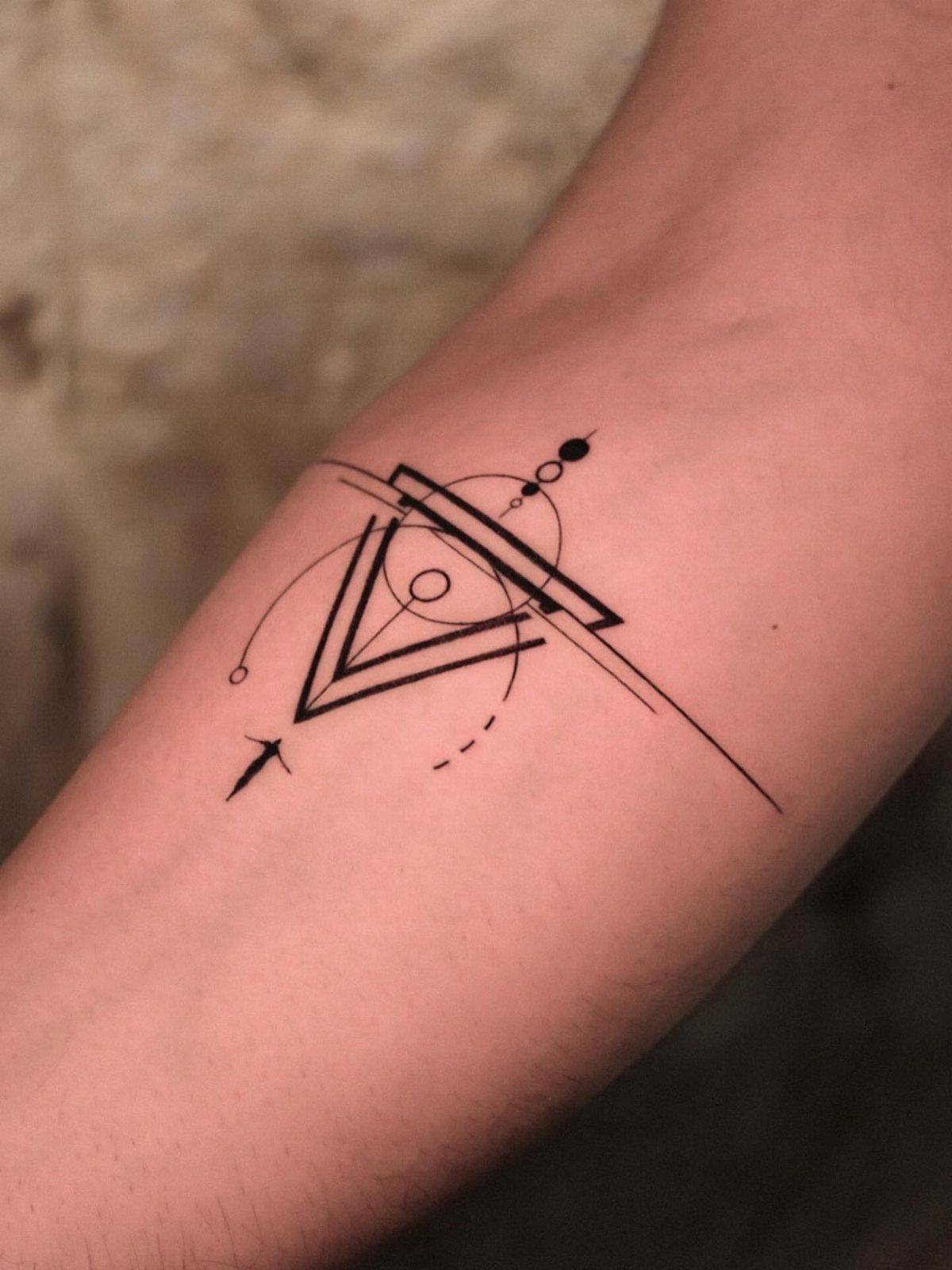 Geometric tattoo on an arm featuring a triangle, circles, and intersecting black lines.