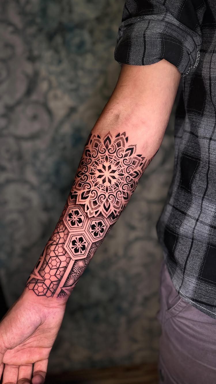 Forearm tattoo featuring a complex mandala and geometric hexagonal patterns in black ink.