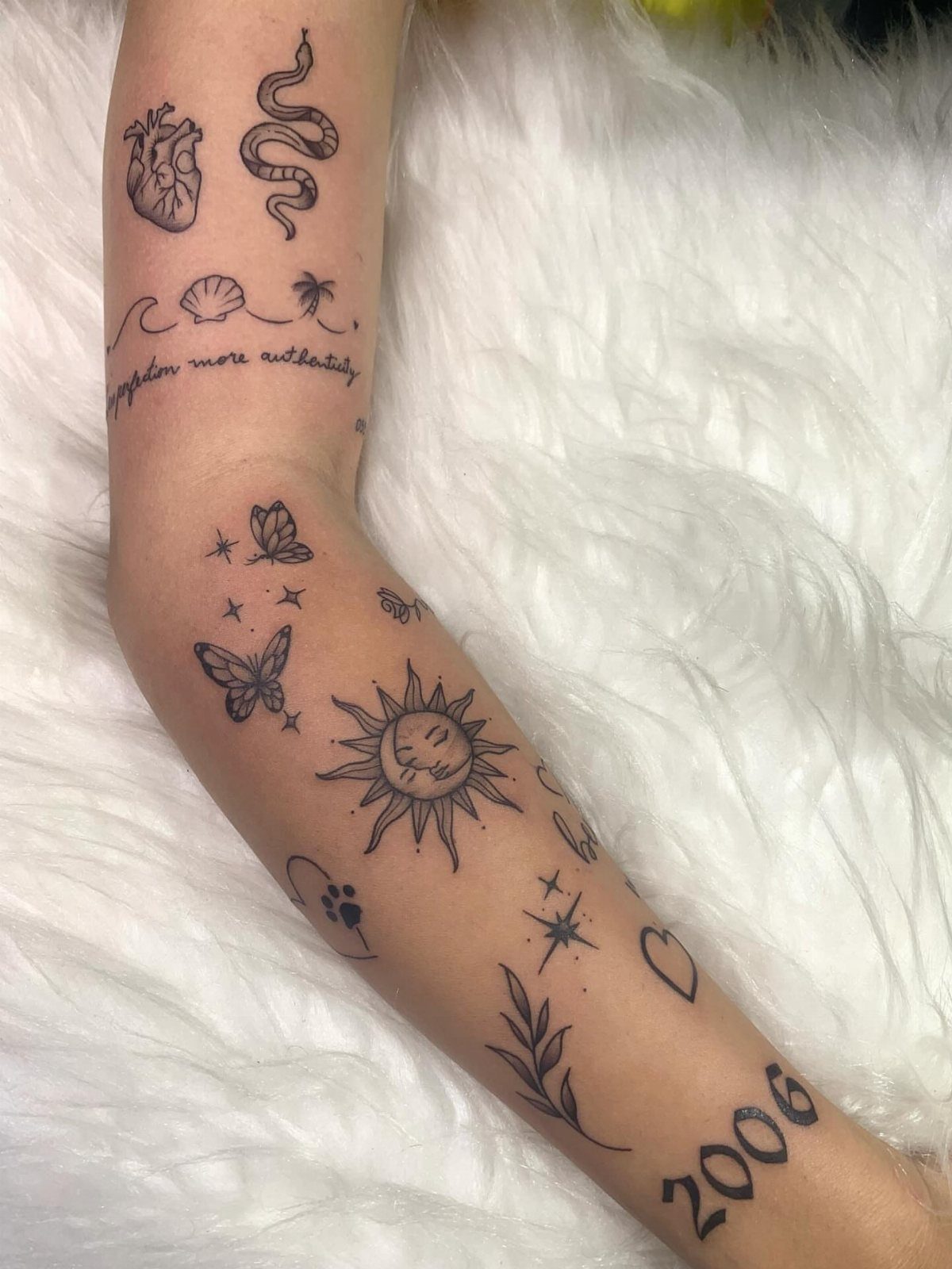 Forearm with various minimalist fine-line tattoos including a sun, butterflies, and a snake.