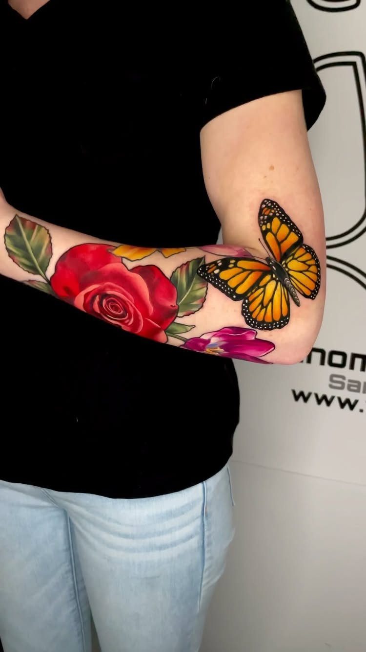 Monarch butterfly and red rose tattoo on a person's forearm