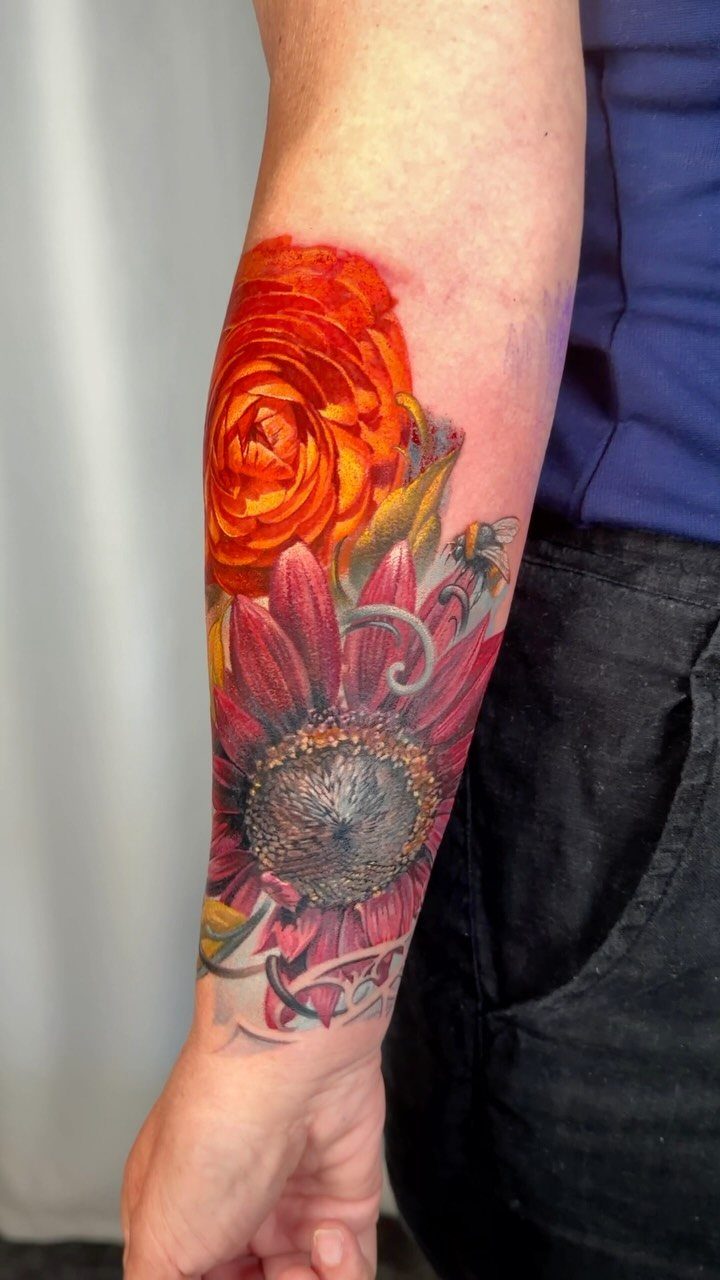 Colorful floral tattoo of an orange rose and red sunflower on a forearm.