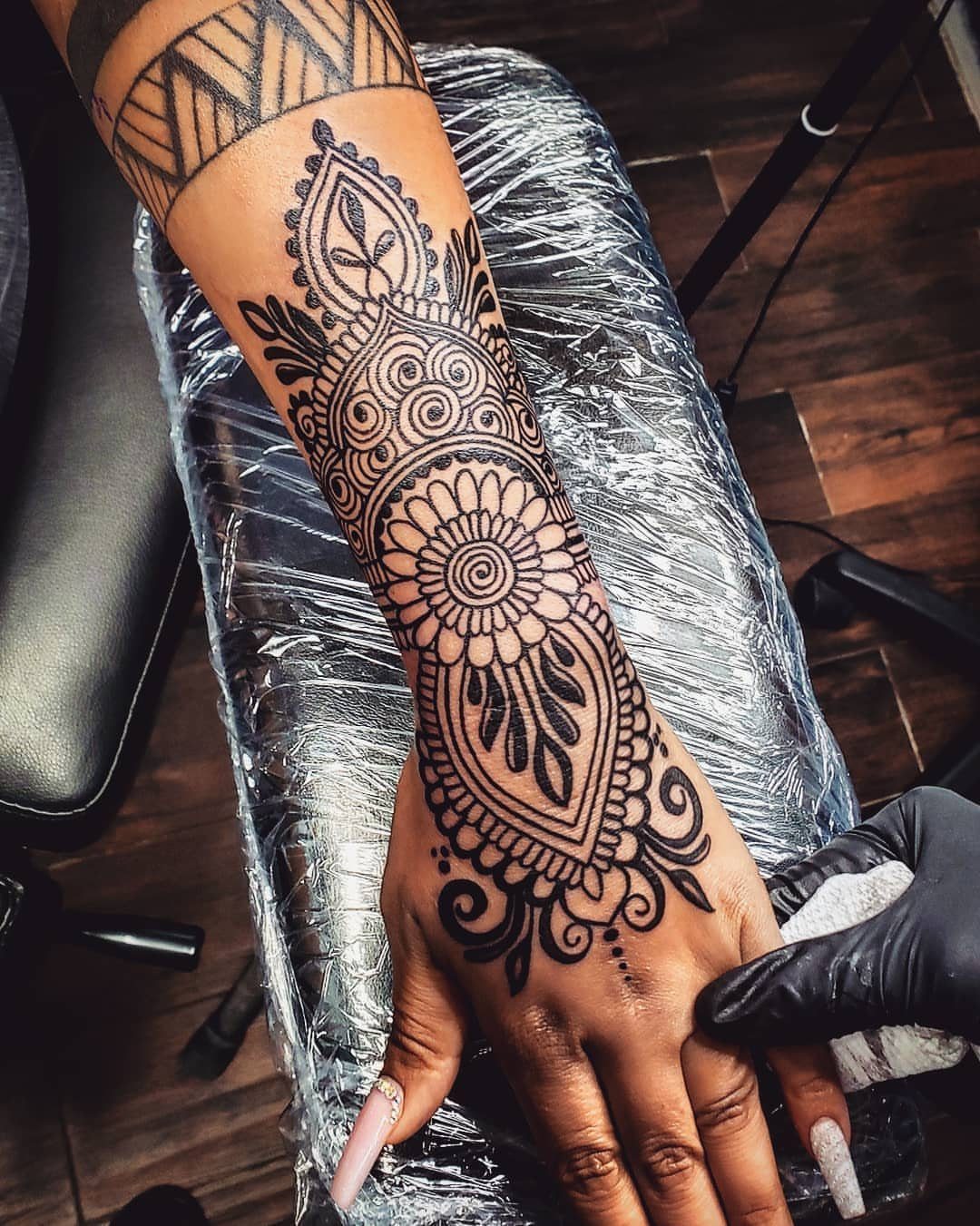 Intricate black ink mandala tattoo on a person's forearm and hand.