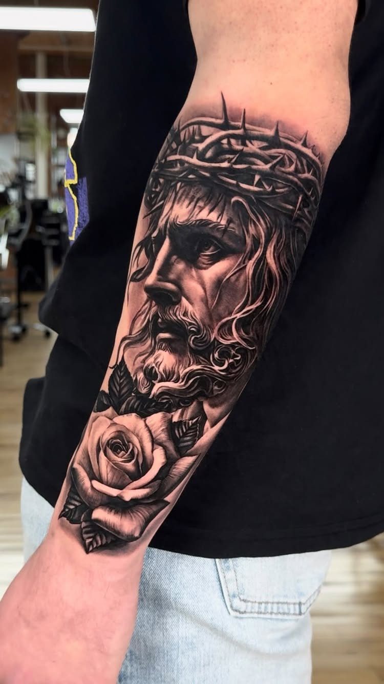 Forearm tattoo featuring a realistic portrait of Jesus with a rose flower below.