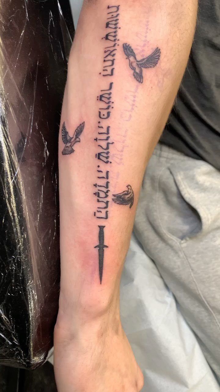 Forearm tattoo with vertical script text, three flying birds, and a small dagger.