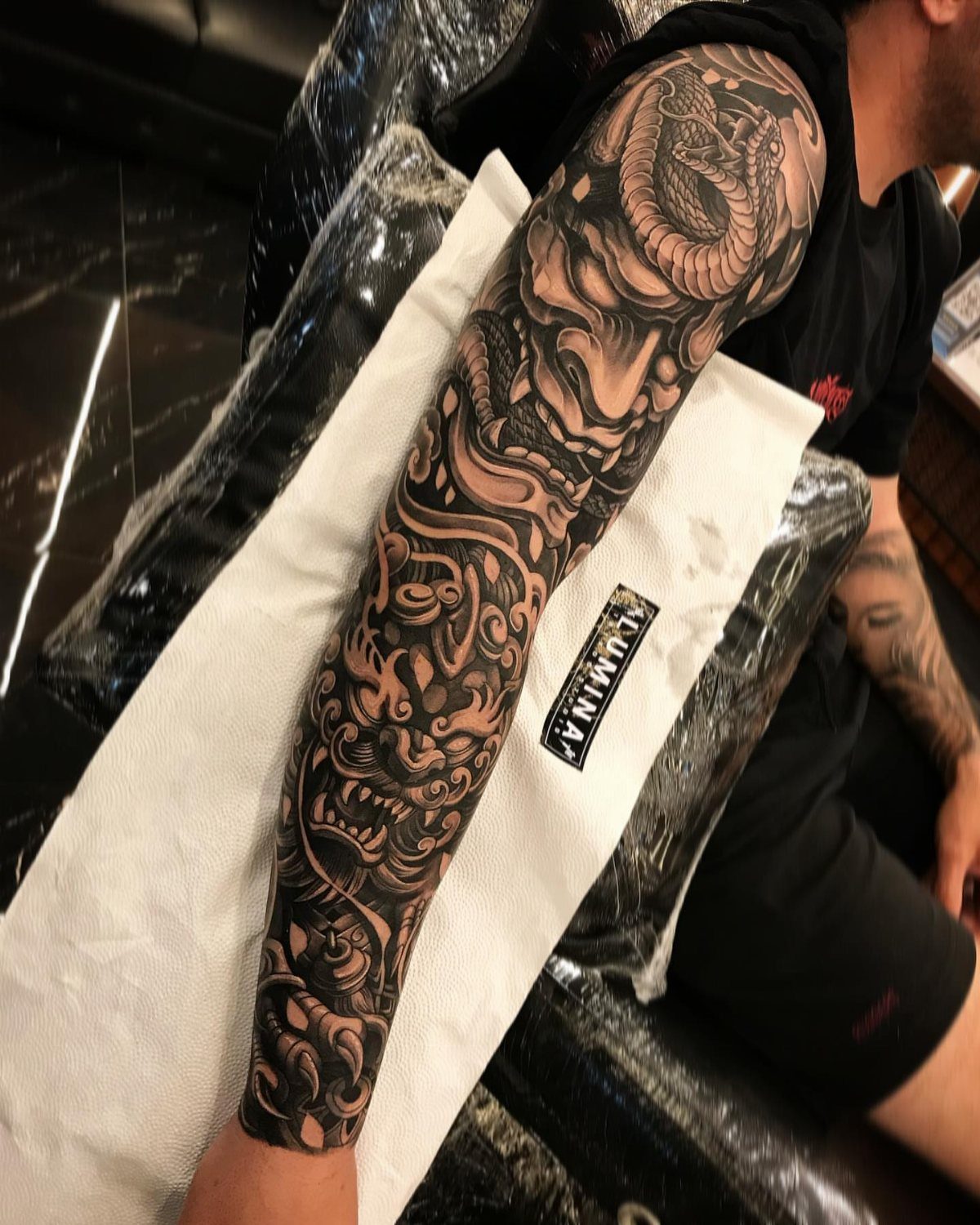 Detailed black and grey dragon and skull tattoo on a man's forearm.