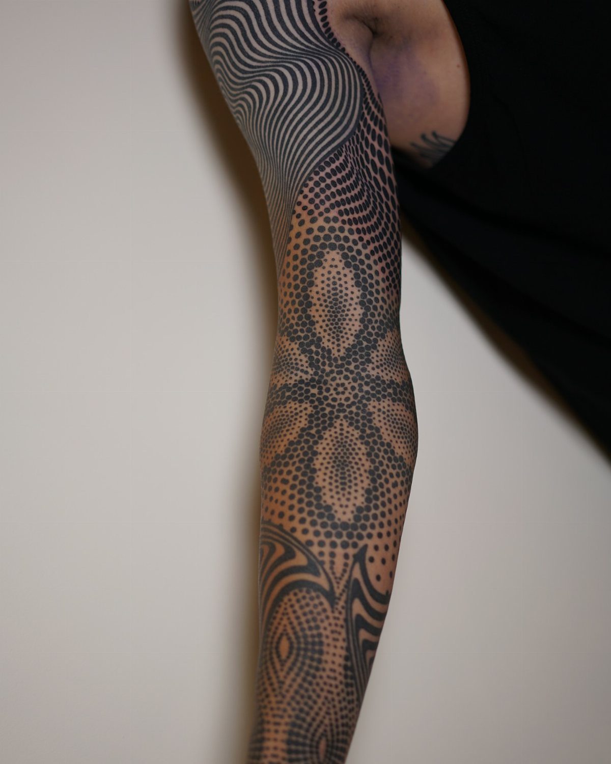 Forearm tattoo with black geometric patterns, dots, and abstract flowing lines.