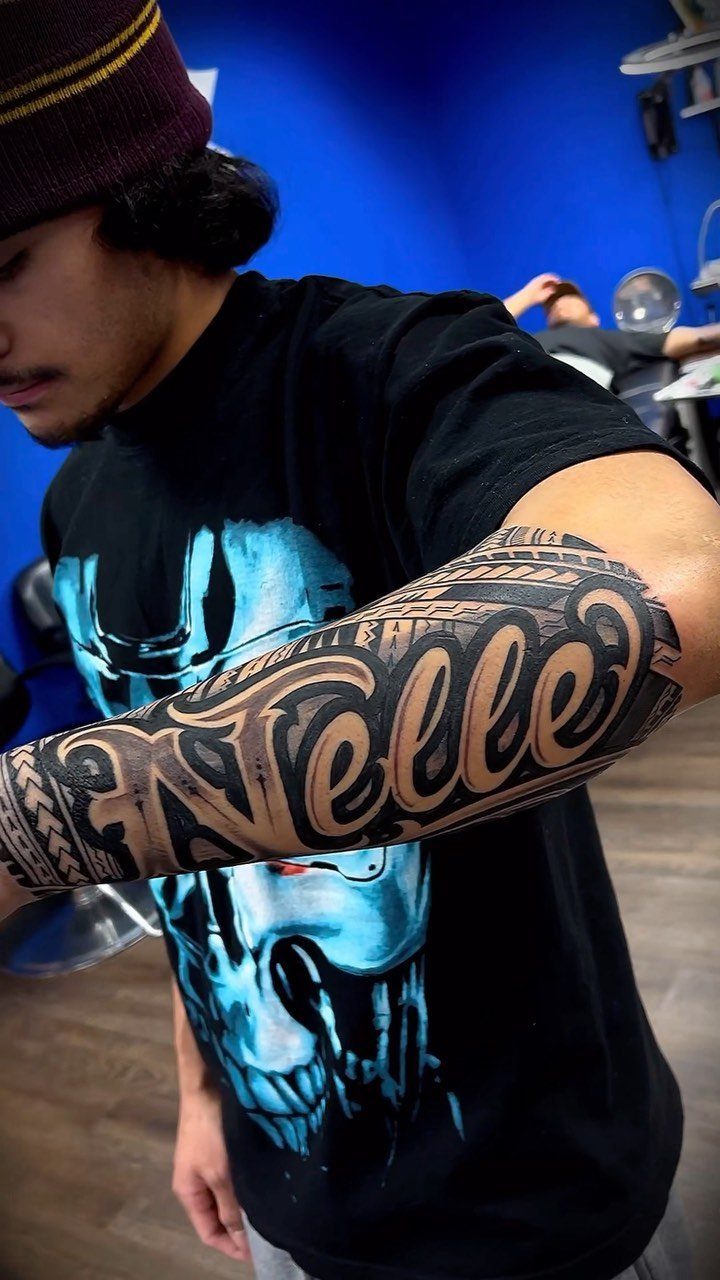 Forearm tattoo with the word Nelle in script surrounded by tribal patterns.