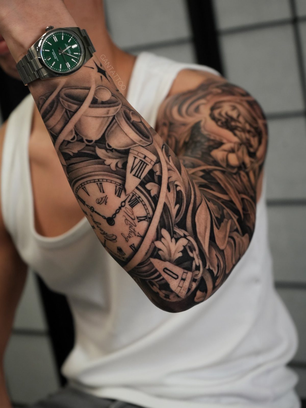 Detailed black and grey sleeve tattoo featuring a clock and a winged portrait.