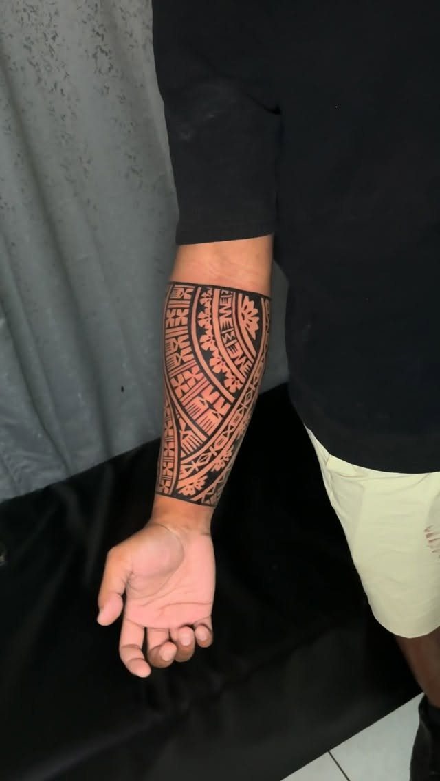 Man's forearm with a detailed black ink tribal tattoo featuring geometric patterns.