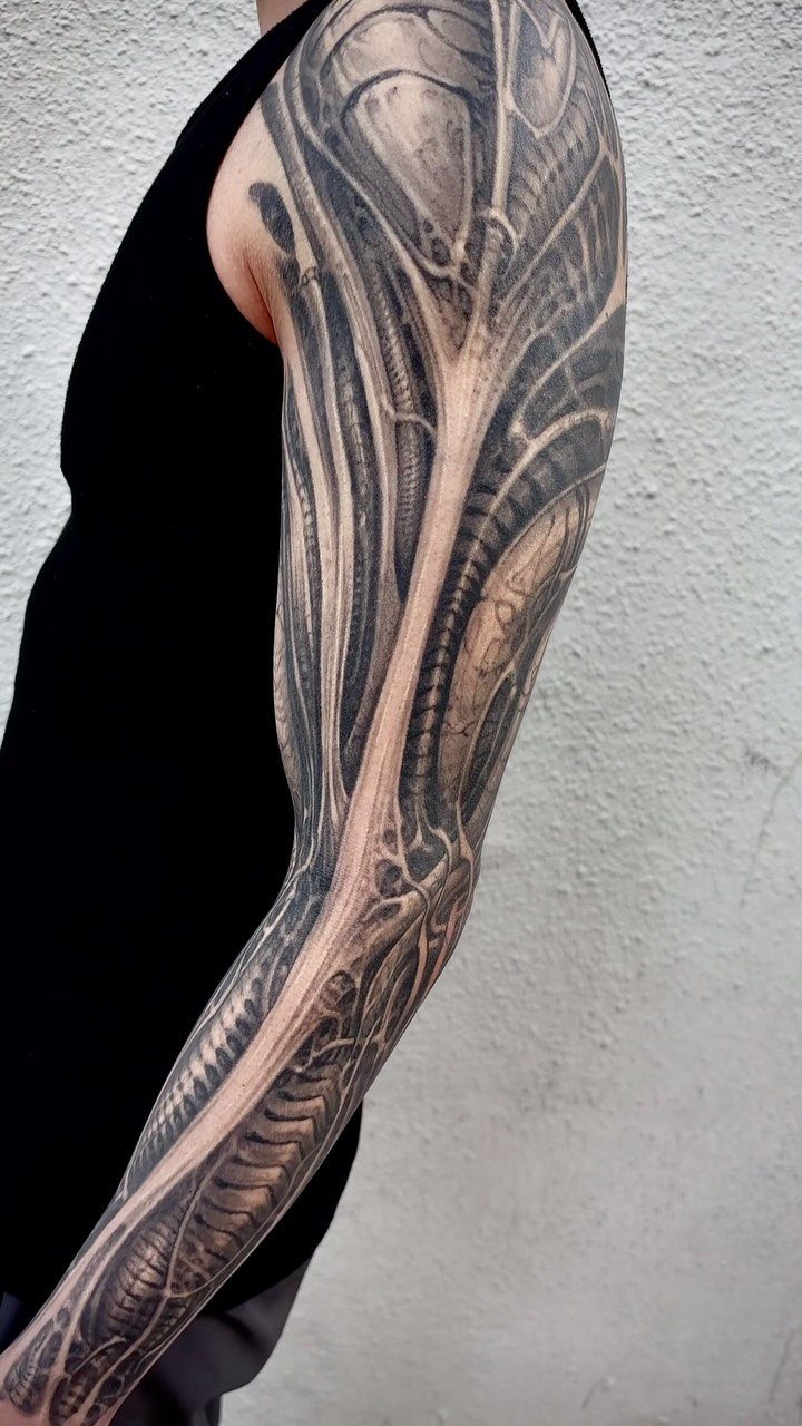 Full sleeve biomechanical tattoo on a man's arm showing detailed mechanical and robotic parts.