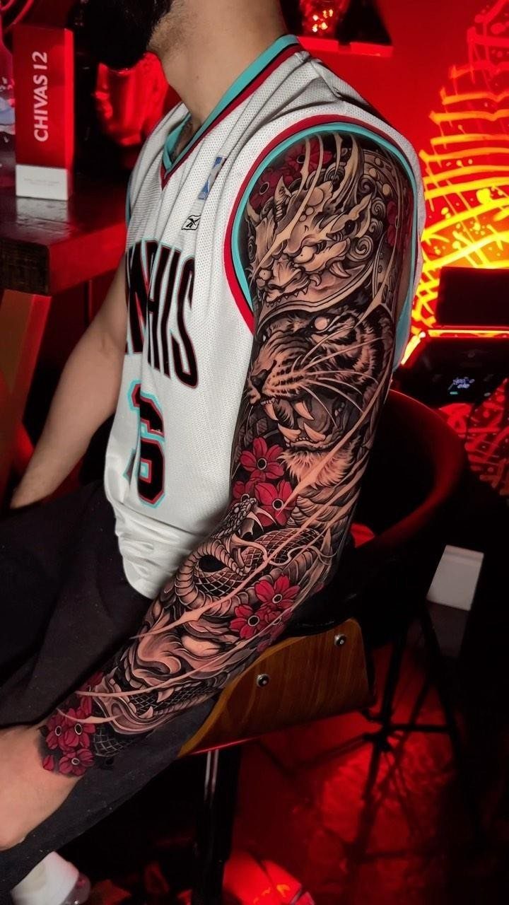 Man with a detailed full arm sleeve tattoo featuring red flowers and dark ink.