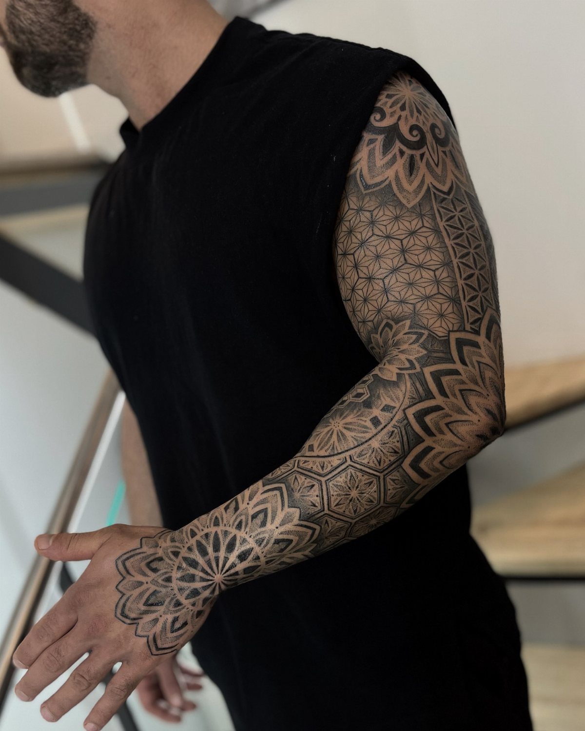 Man with a full sleeve tattoo featuring intricate black geometric and mandala patterns.
