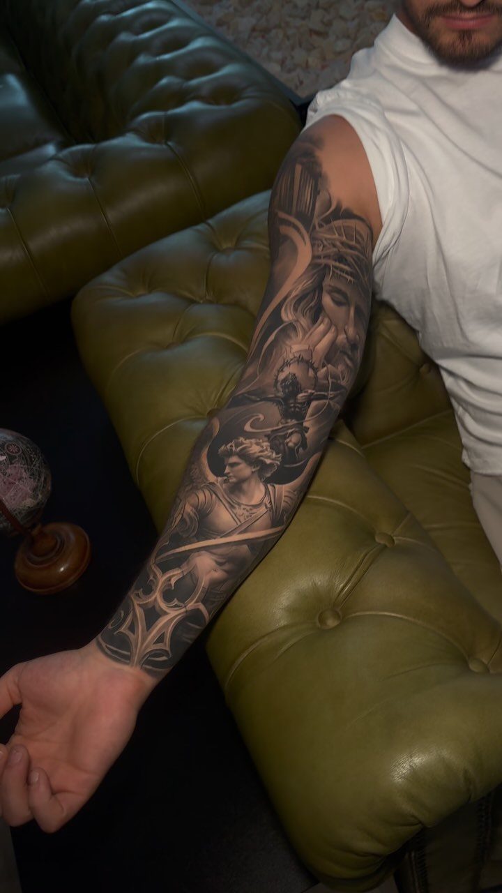Man's arm with a detailed black and grey full sleeve tattoo on a sofa