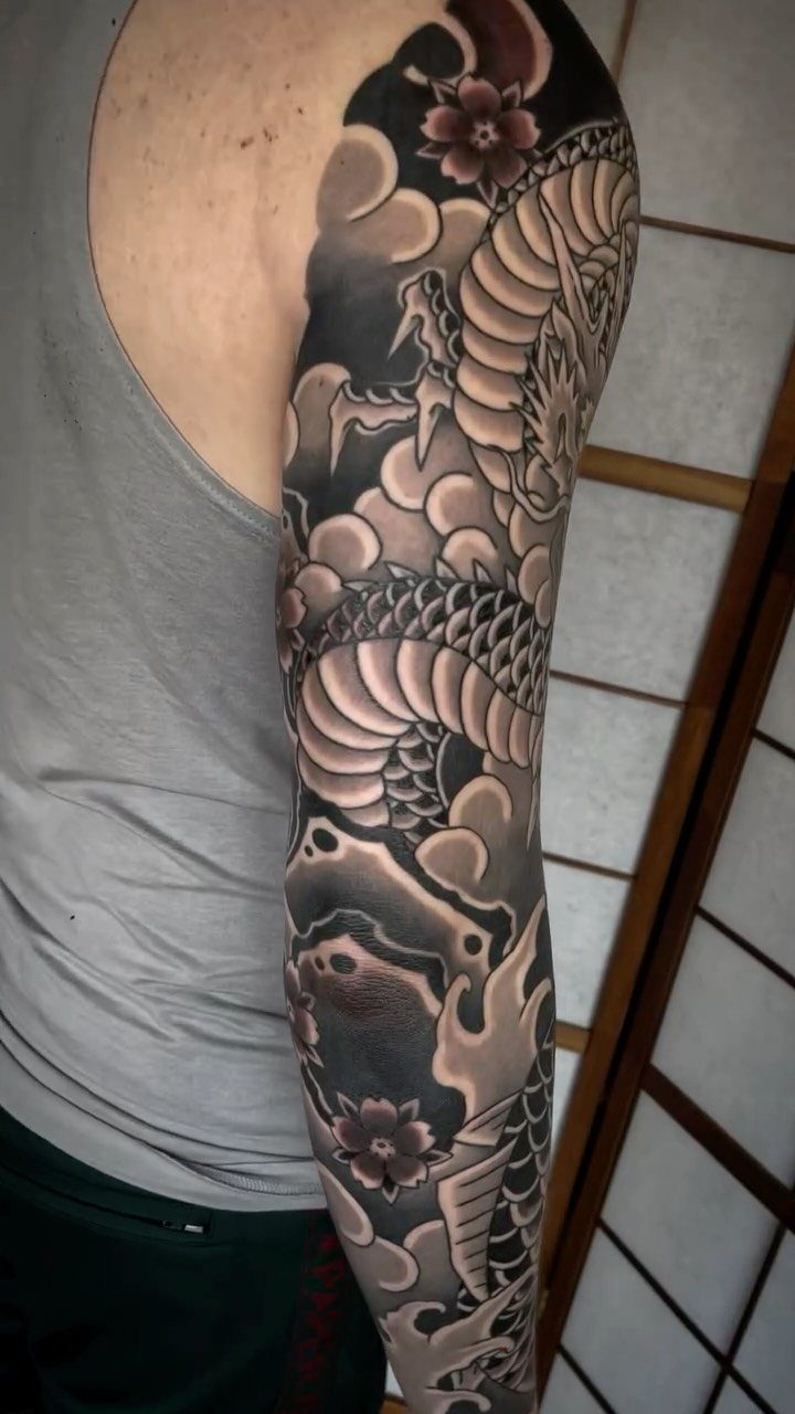 Full sleeve tattoo on a man's arm featuring a Japanese dragon and clouds.
