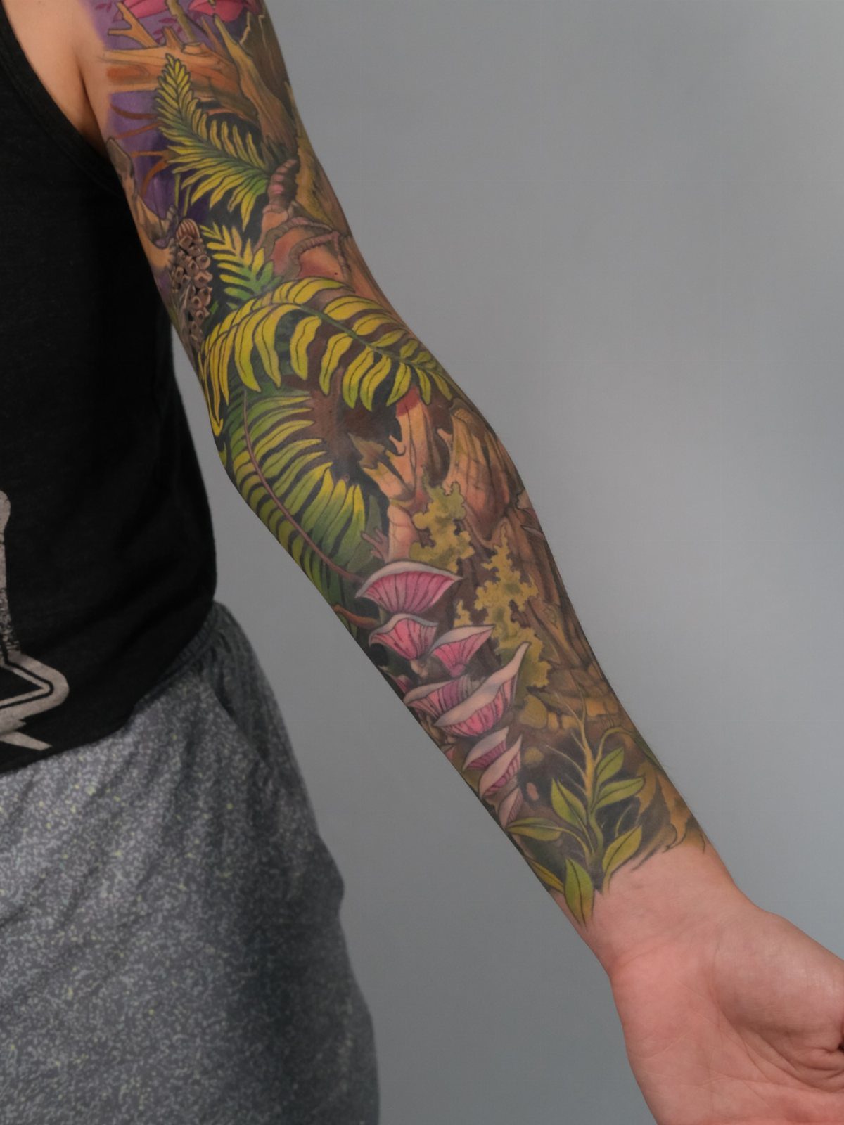 Full sleeve tattoo of a forest with ferns and mushrooms on a man's arm.
