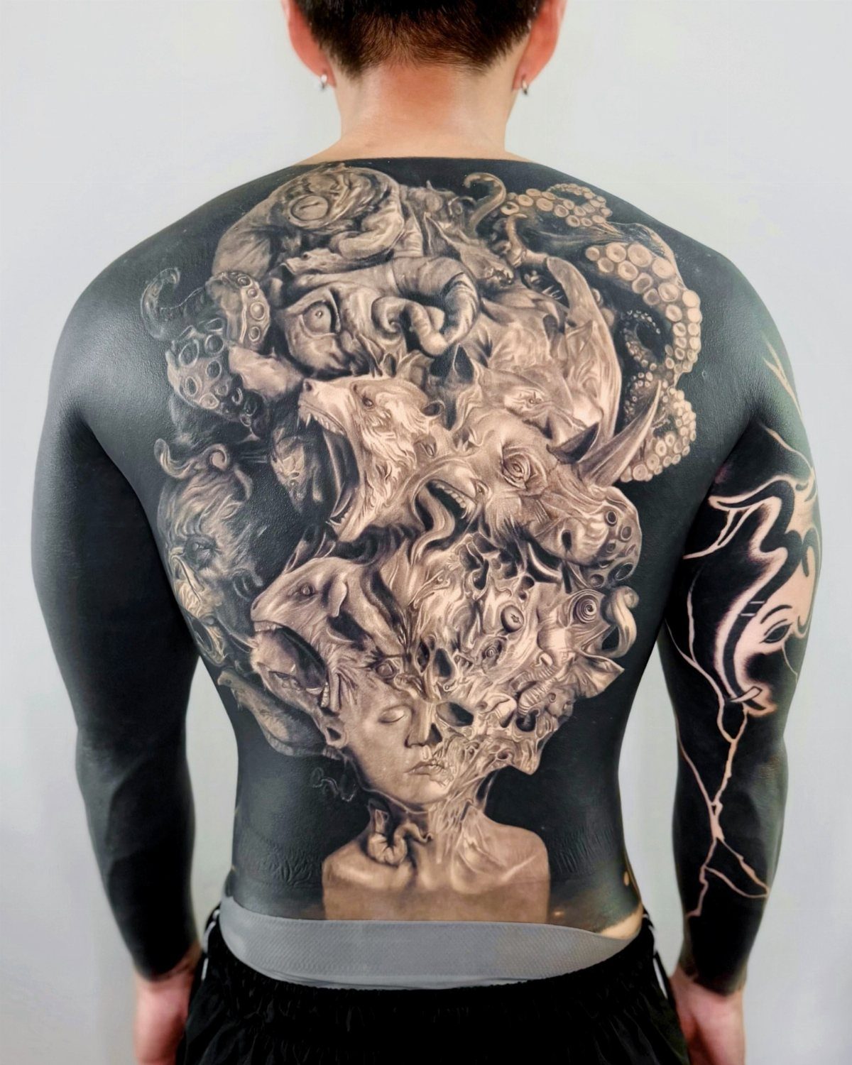 Surreal 3D grayscale tattoo on a person's back featuring distorted faces and organic forms.